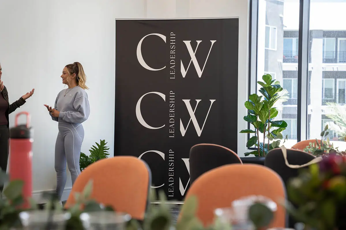 Two women talking beside the Collective Women's Leadership banner at a CWL gathering
