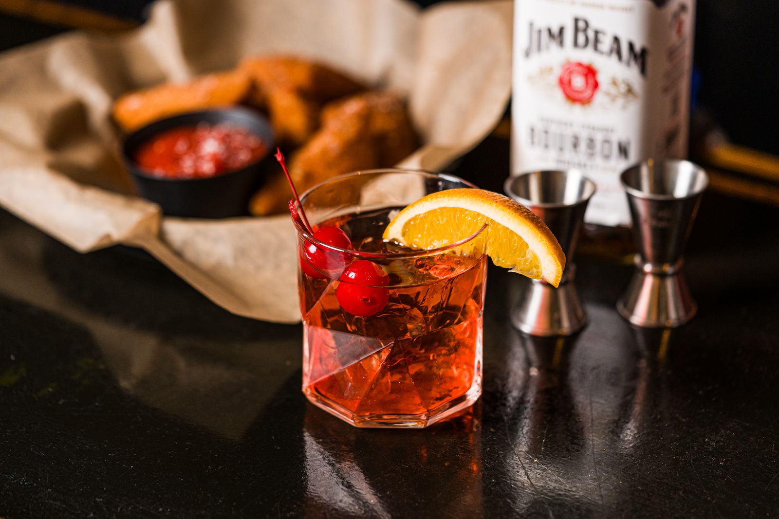 Old fashioned cocktail with a bourbon bottle behind the bar