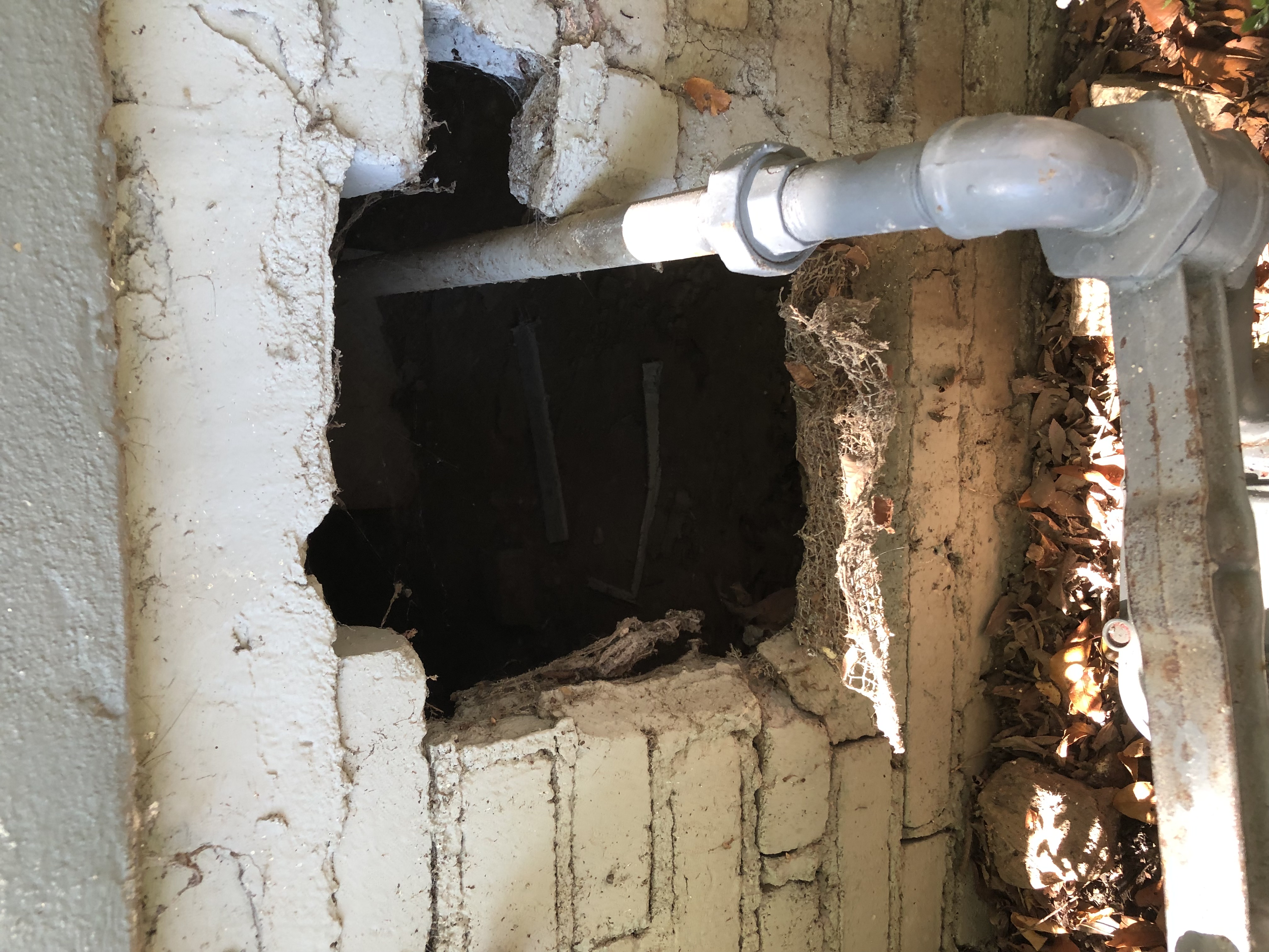 The same foundation wall before the work, with an open wildlife entry hole beside a pipe