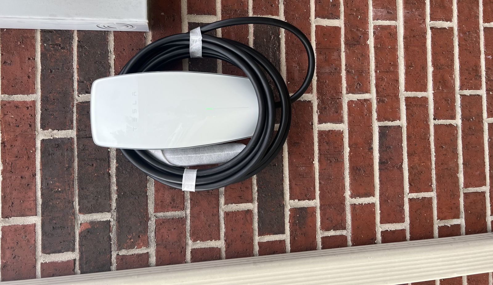 Tesla Wall Connector mounted on a brick exterior wall beside the service equipment