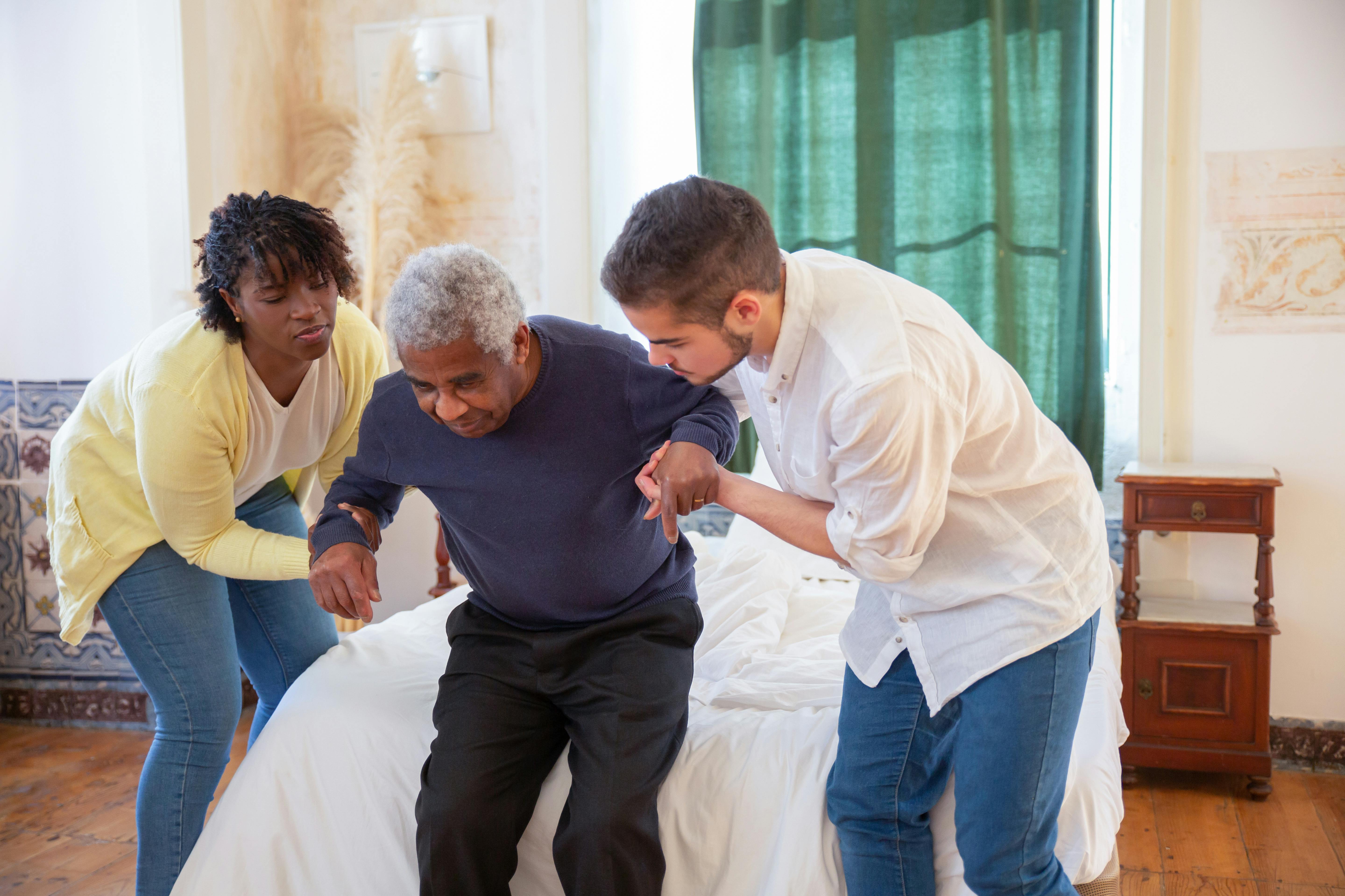 Caregivers assisting elderly man with mobility support getting out of bed, in-home senior care and assisted living support concept Caregivers assisting elderly man with mobility support getting out of bed, in-home senior care and assisted living support concept
