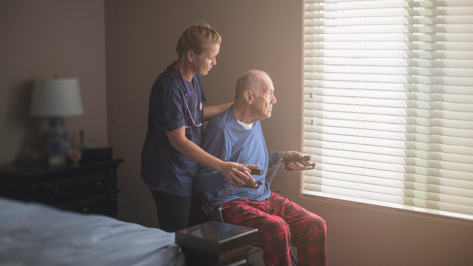Elderly man looking out window with care work Elderly man looking out window with care work