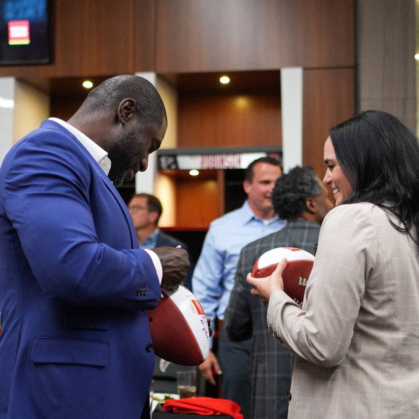Ovie Mughelli handing signed footballs to a guest at an event
