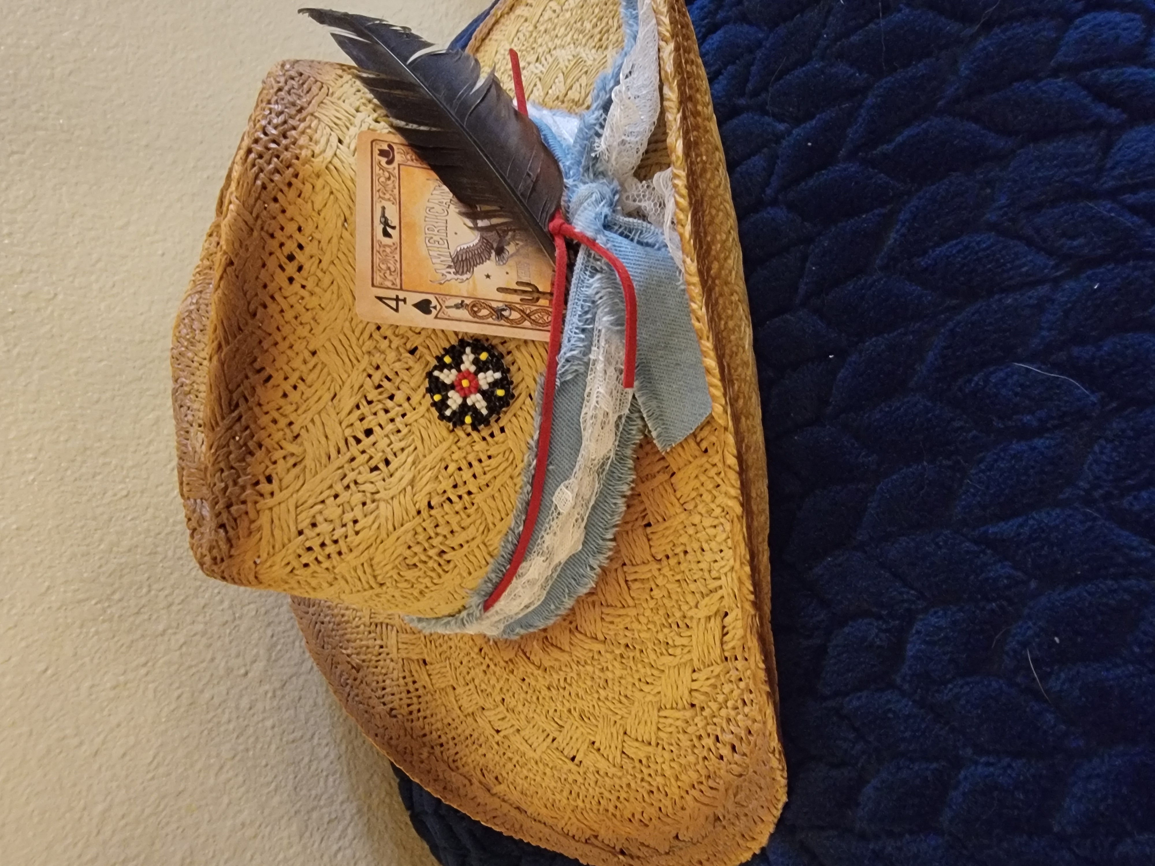 Straw hat decorated with a denim band, feather, and beaded concho