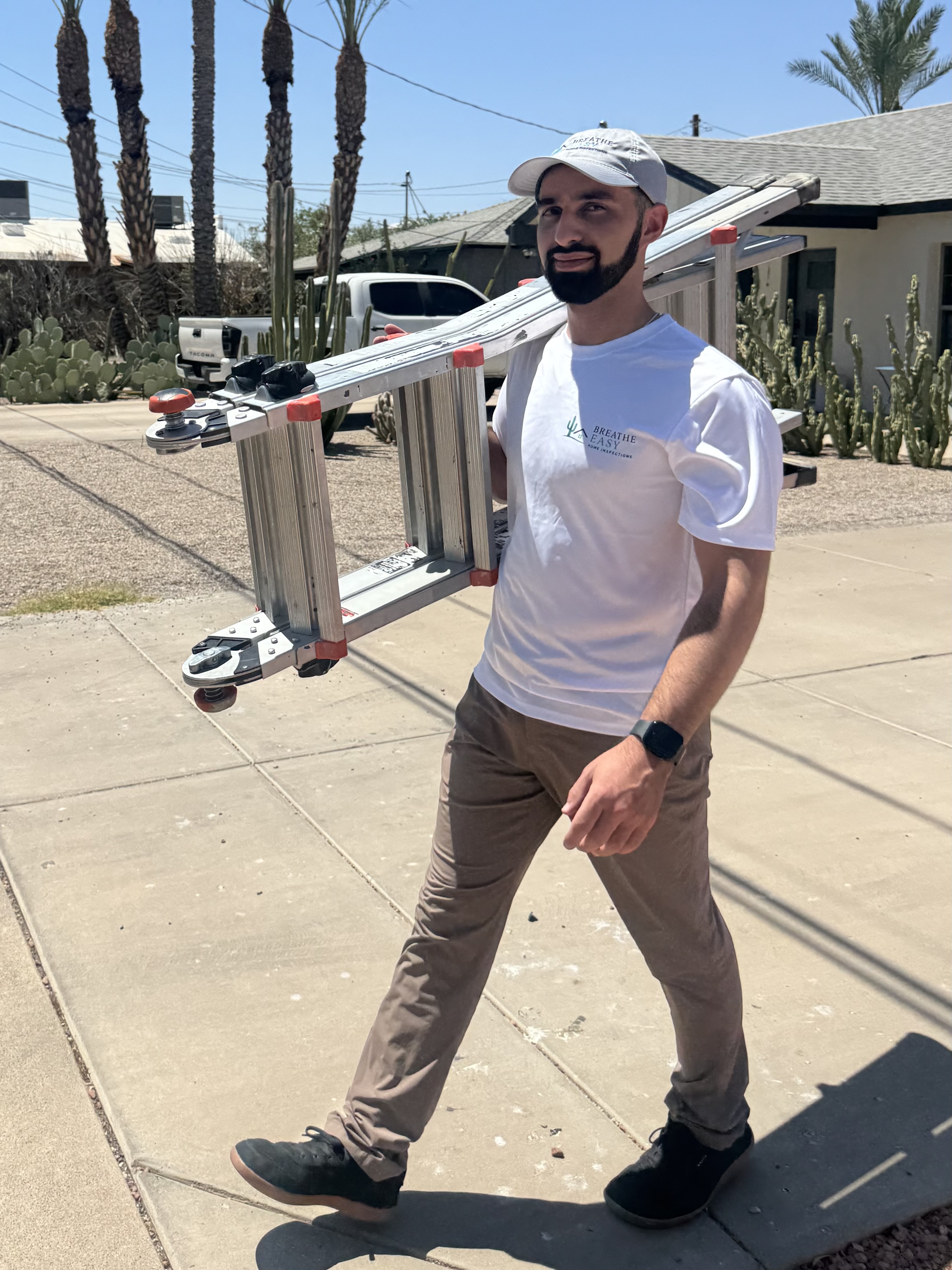 Konnor carrying a ladder down a desert neighborhood sidewalk