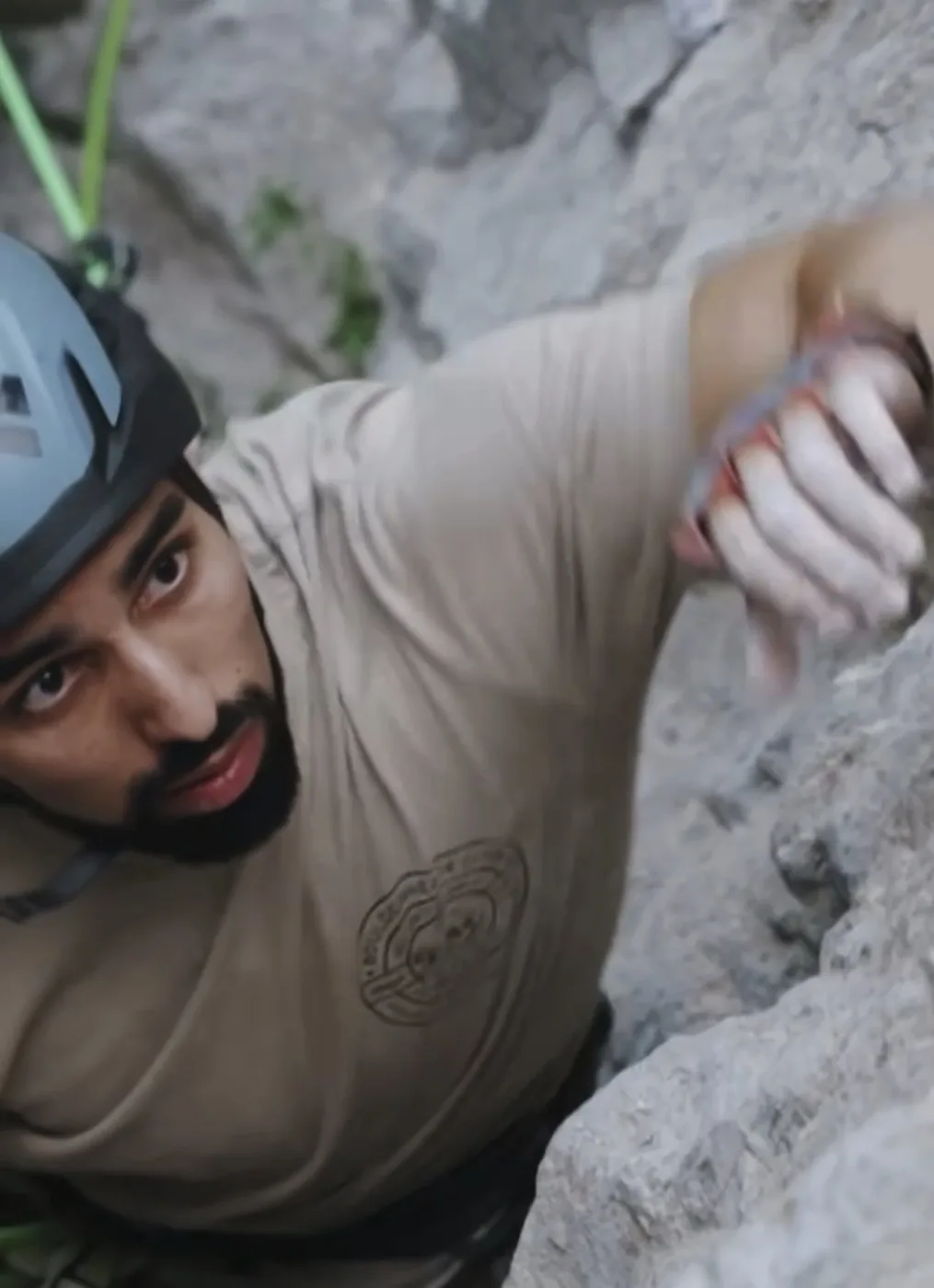 Konnor rock climbing, helmet on, hand gripping a hold
