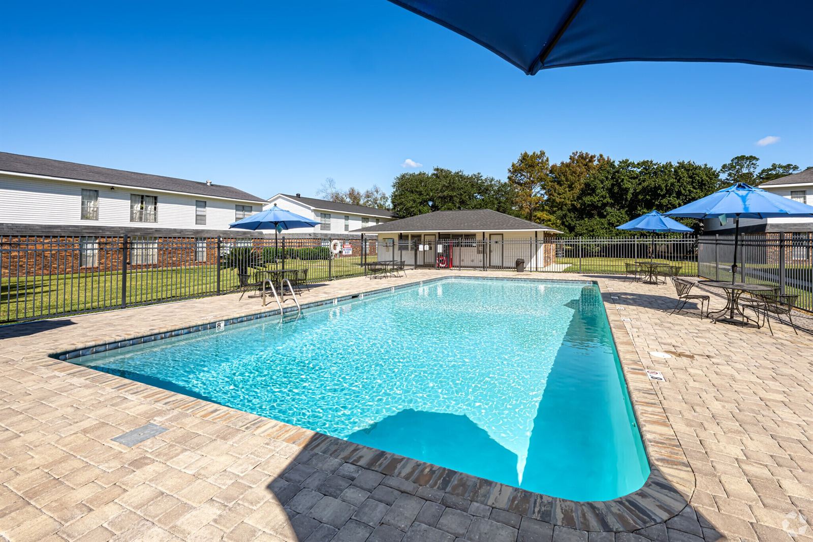 Swimming pool with paver sundeck, tables and blue umbrellas