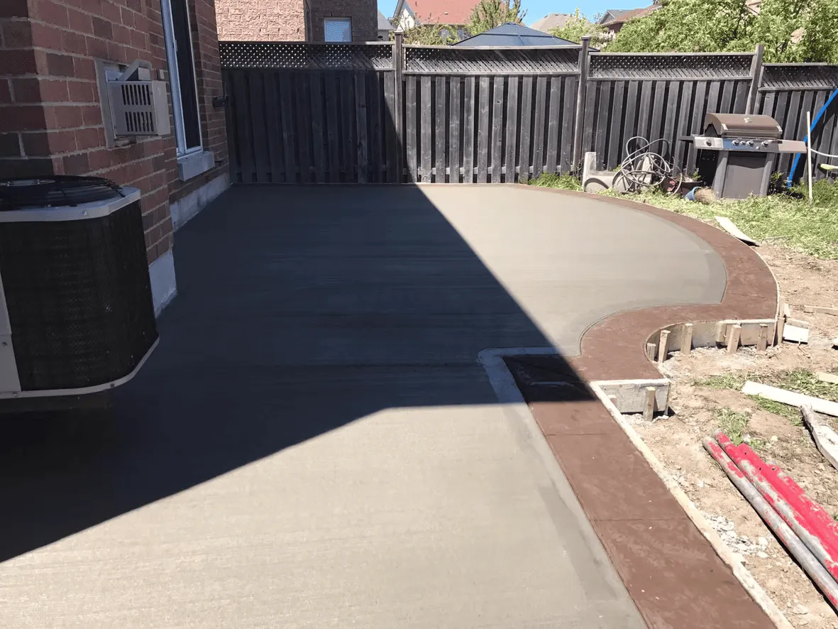 Curved plain concrete backyard patio with a coloured border