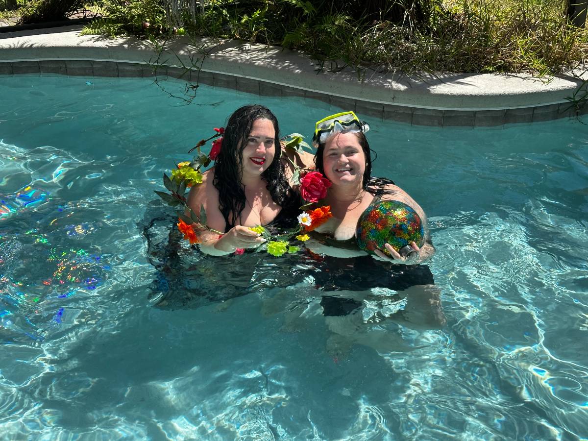 Two women laughing in the pool, dressed in flowers
