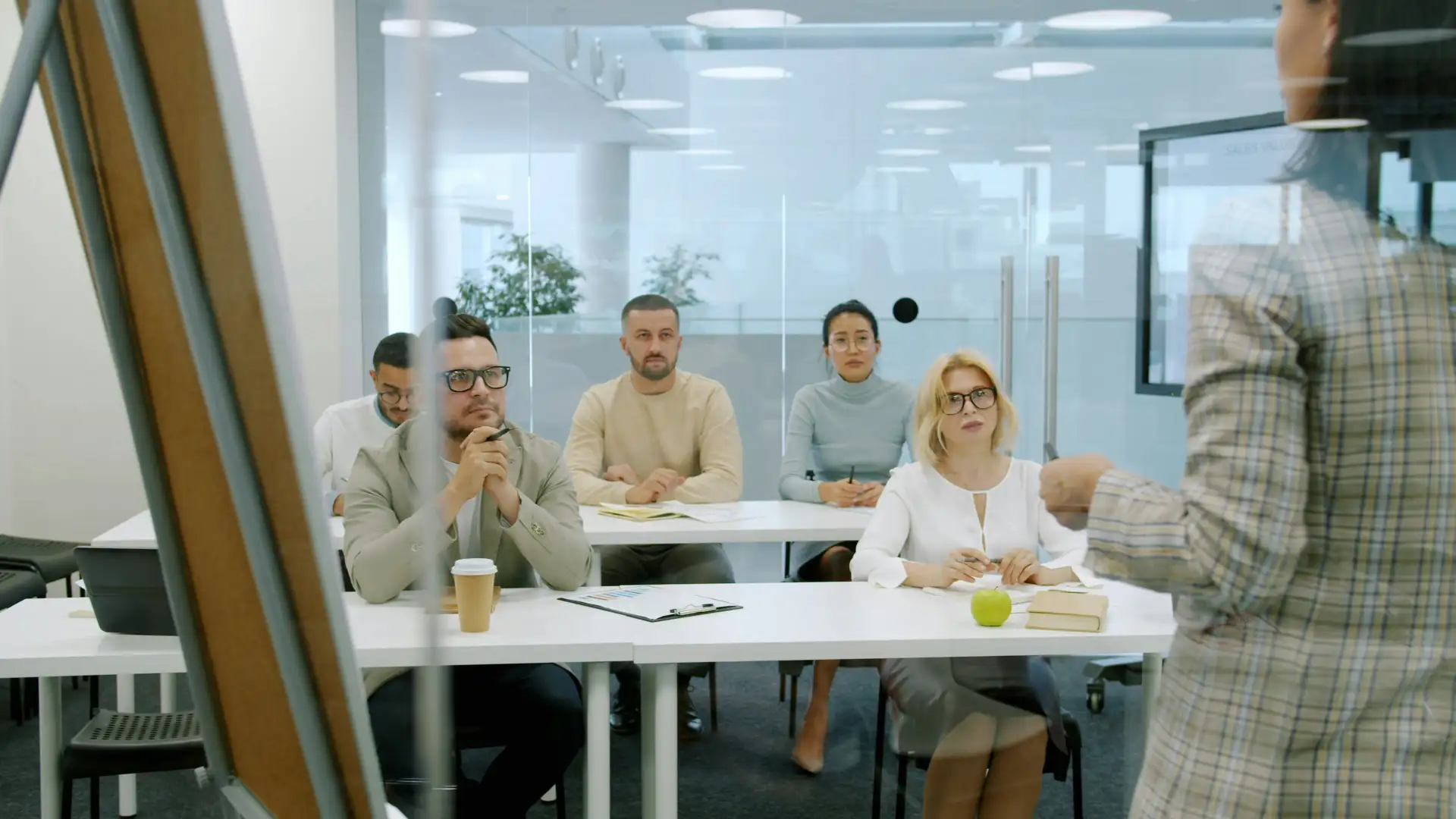 Group of colleagues watching quietly as a presenter speaks at the front of a meeting room. Group of colleagues watching quietly as a presenter speaks at the front of a meeting room.