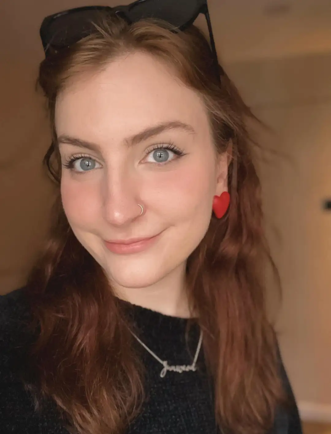 Close-up portrait of Jane Hargrave smiling with sunglasses on her head, red heart earrings, and a necklace