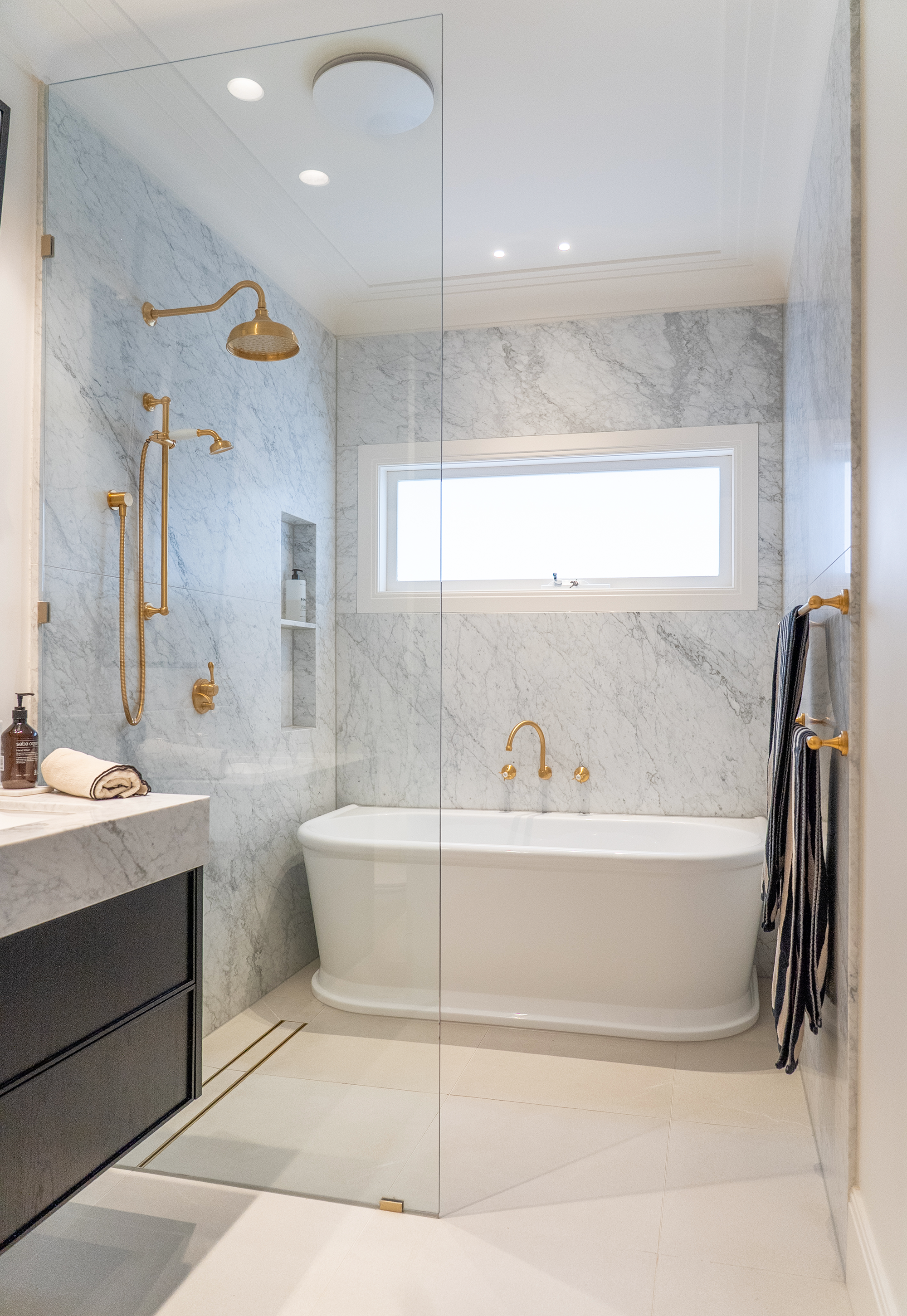 Bathroom renovation Melbourne with freestanding bathtub, walk-in shower, marble walls, and brass fixtures