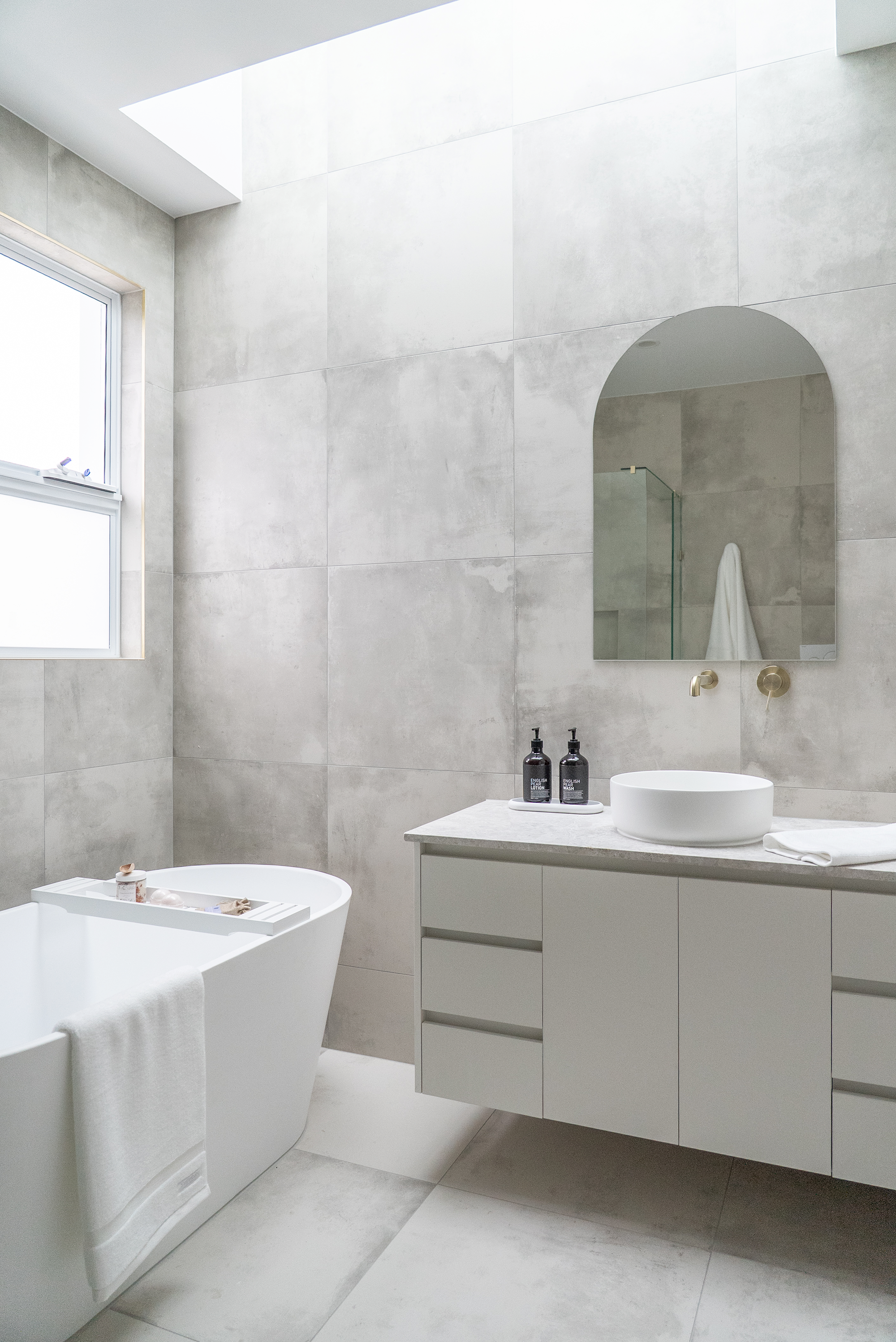 Bathroom renovation Melbourne with freestanding bathtub, vanity, arched mirror, and natural light design