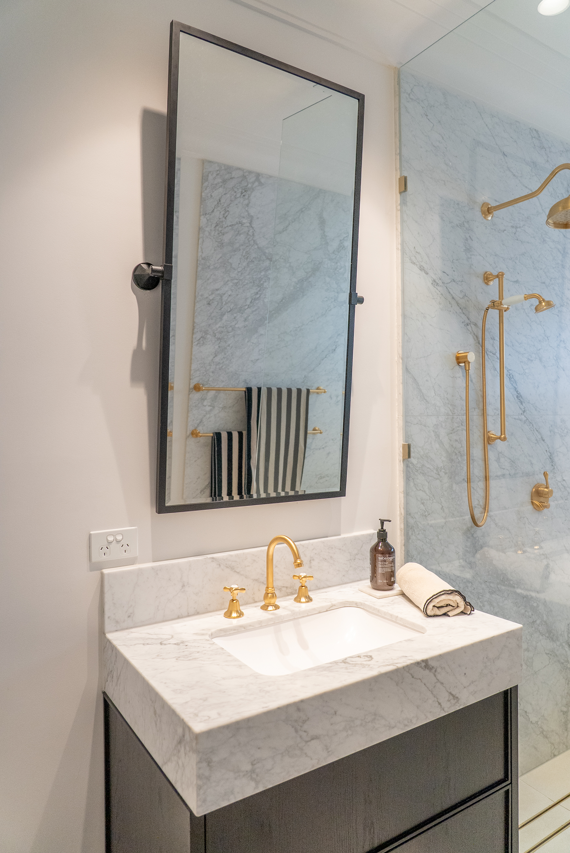 Bathroom renovation Melbourne vanity with mirror, marble benchtop, brass tapware, and walk-in shower
