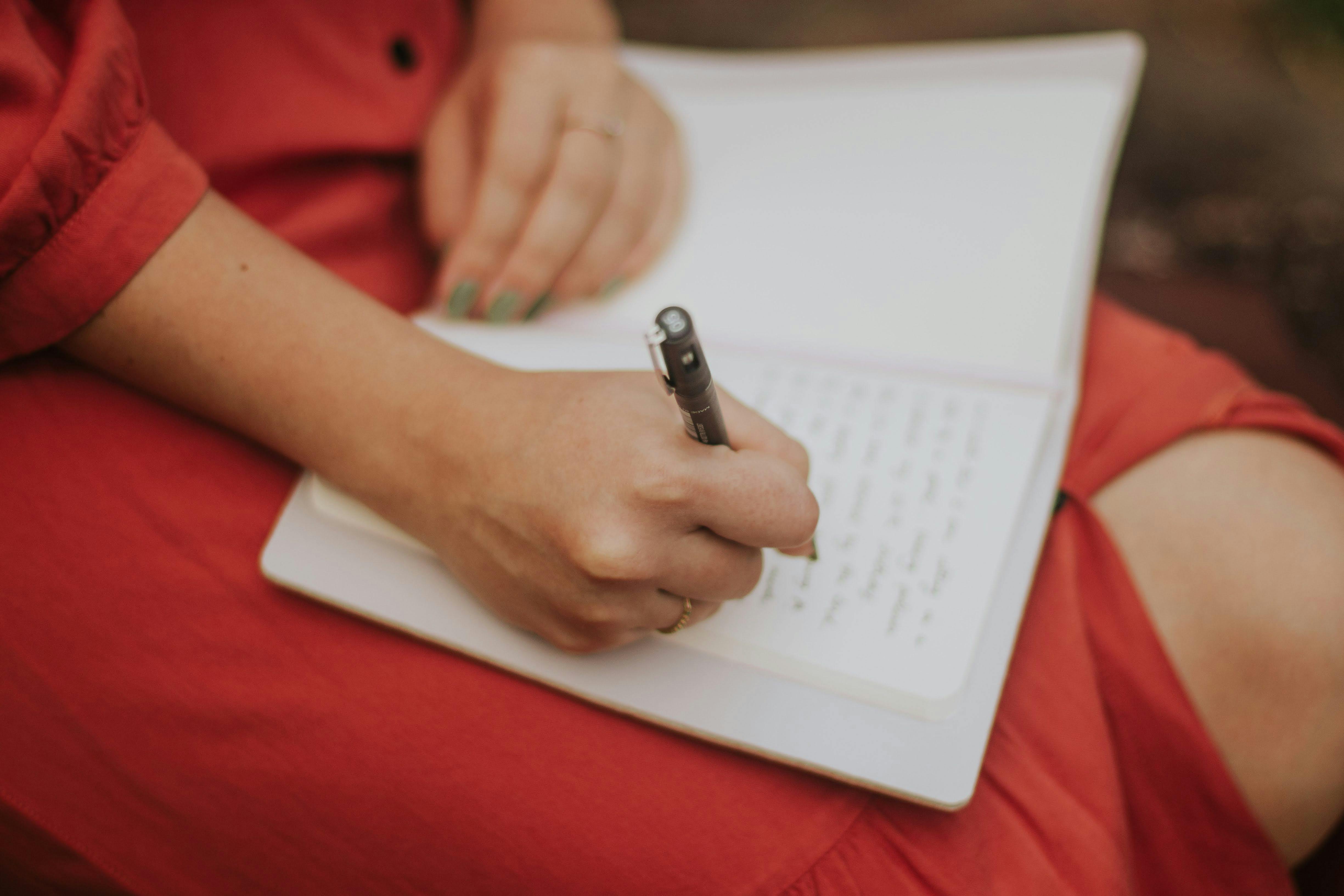 Woman in a red dress writing in a journal, representing symptom tracking, reflection, and mindful health habits during perimenopause and gut healing.