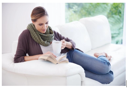 Woman relaxing on a couch with tea and a book, supporting stress management and healthy habits during perimenopause