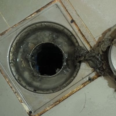 Dirty floor drain with visible buildup and clogging debris in need of cleaning