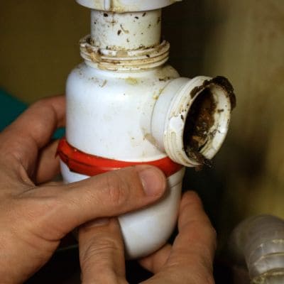 Plumber removing a clogged trap from a sink pipe to clear debris buildup