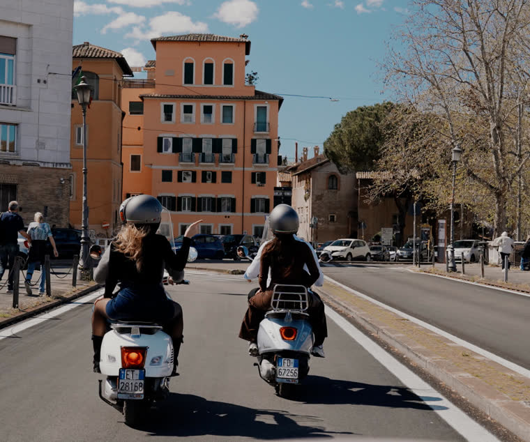 Two Vespas riding down a sunlit street in Rome