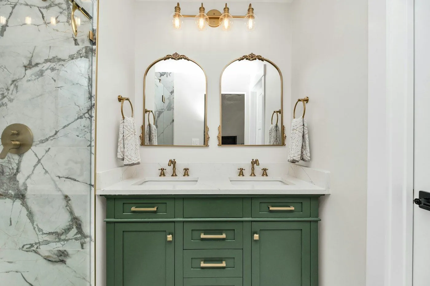 A bathroom with a green double vanity, marble counter and brass mirrors