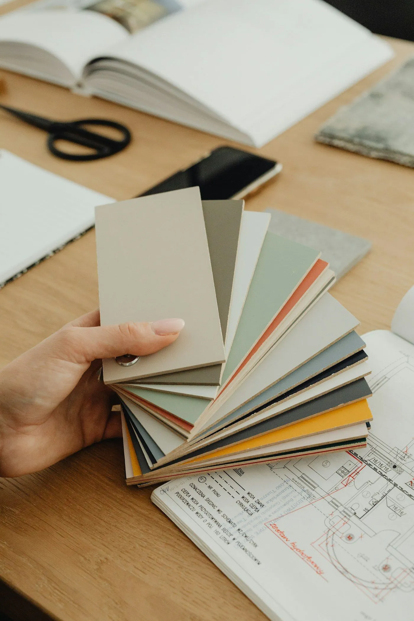 A hand holding a fan of colour swatches over a set of plans