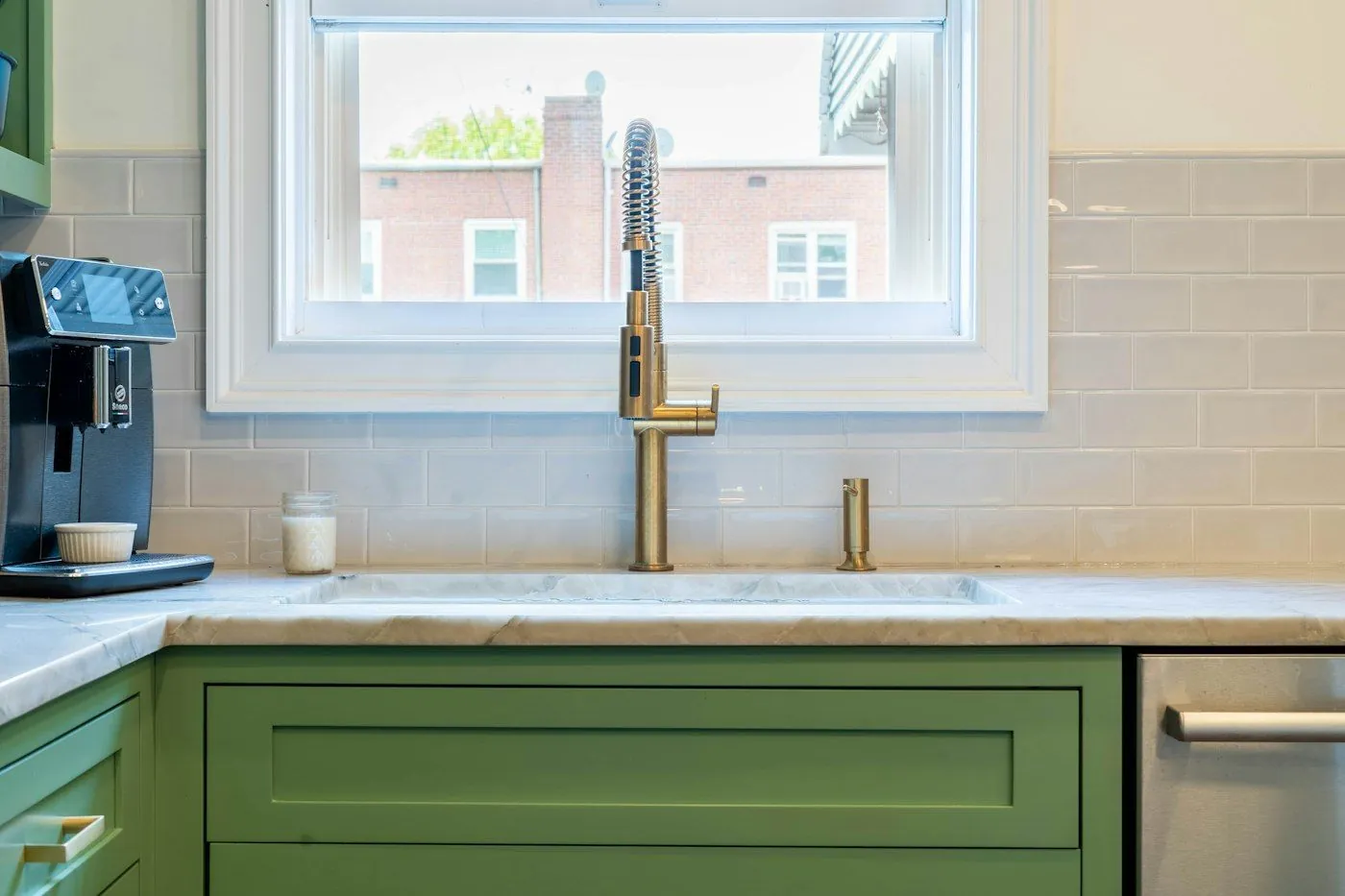 Green kitchen cabinets with a brass faucet under a window