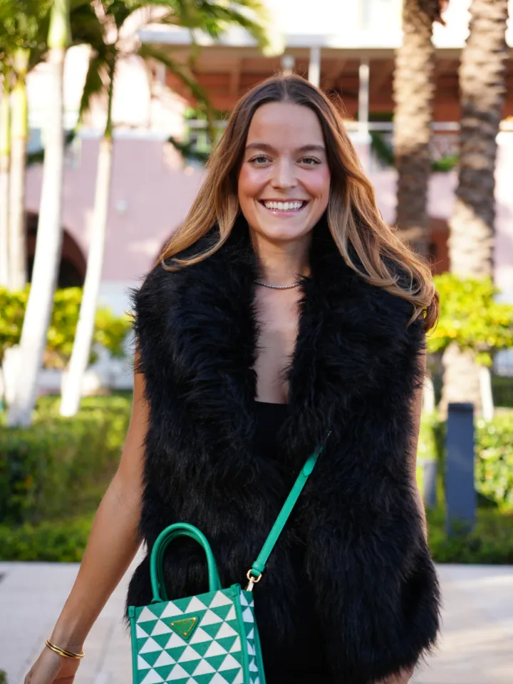 Steph Currie smiling in a black faux fur vest under the palm trees in St. Petersburg, Florida