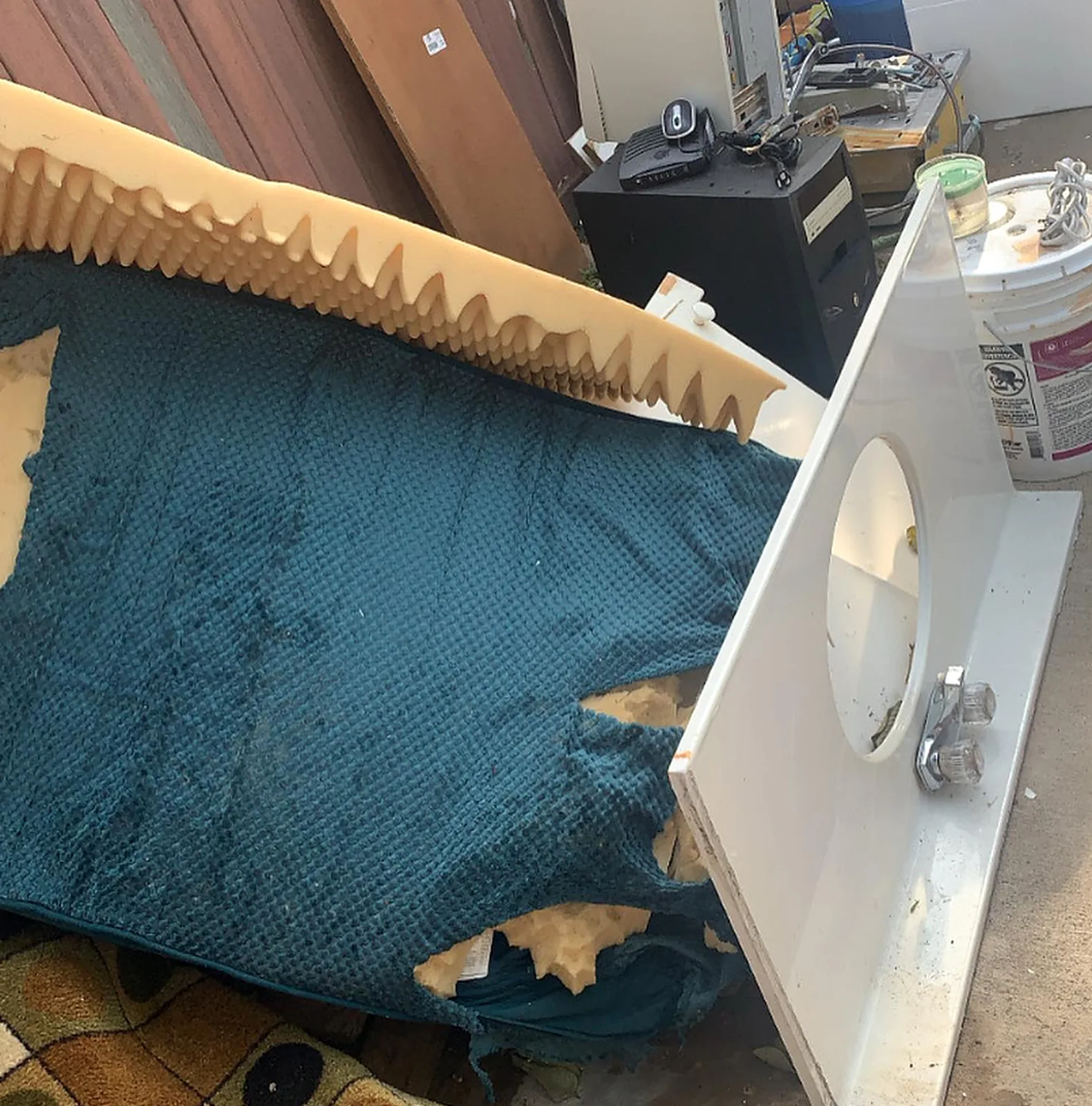 A pile of junk: a foam mattress topper, a rug, a bathroom vanity top, a computer and buckets.