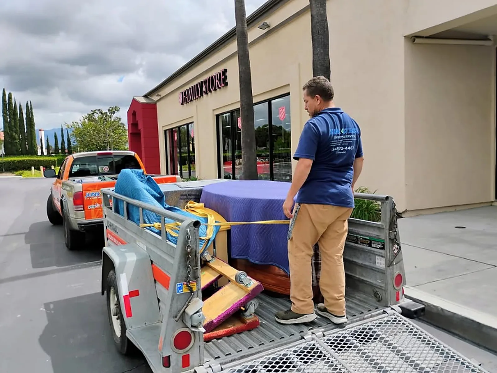 A loaded trailer outside a thrift store, with a person in a Junk Stars shirt and the Junk Stars truck behind.