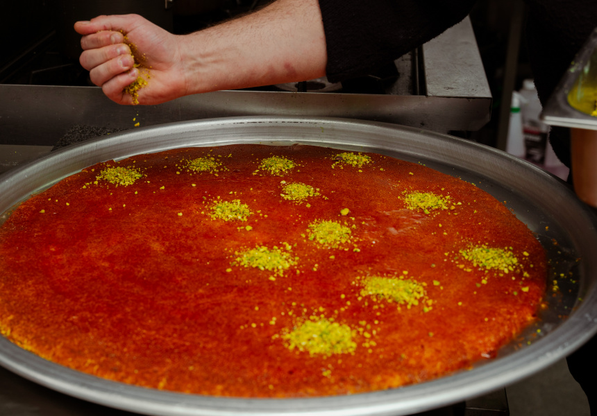 Dramatic cheese pull from a freshly served tray of golden knafeh nabulseyeh at an event