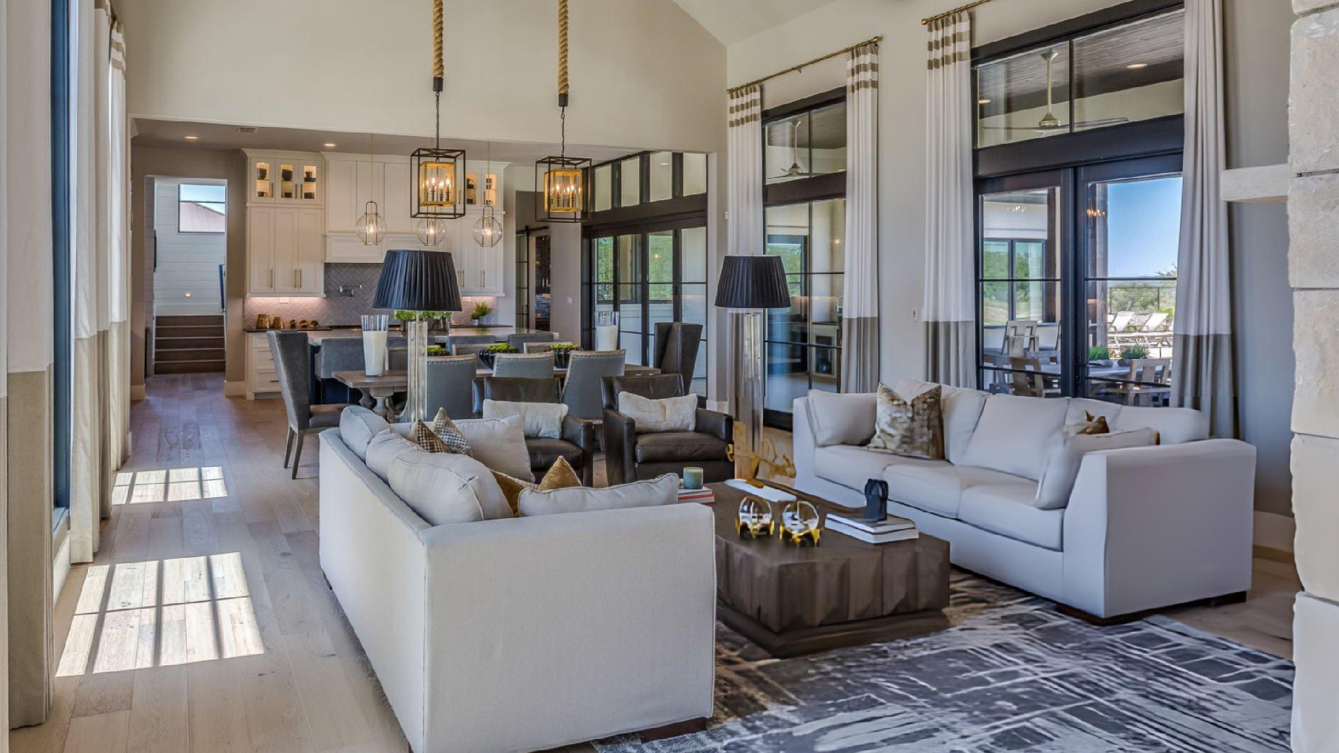 Modern luxury living room with open kitchen, elegant furnishings, large windows, and bright natural light inside.