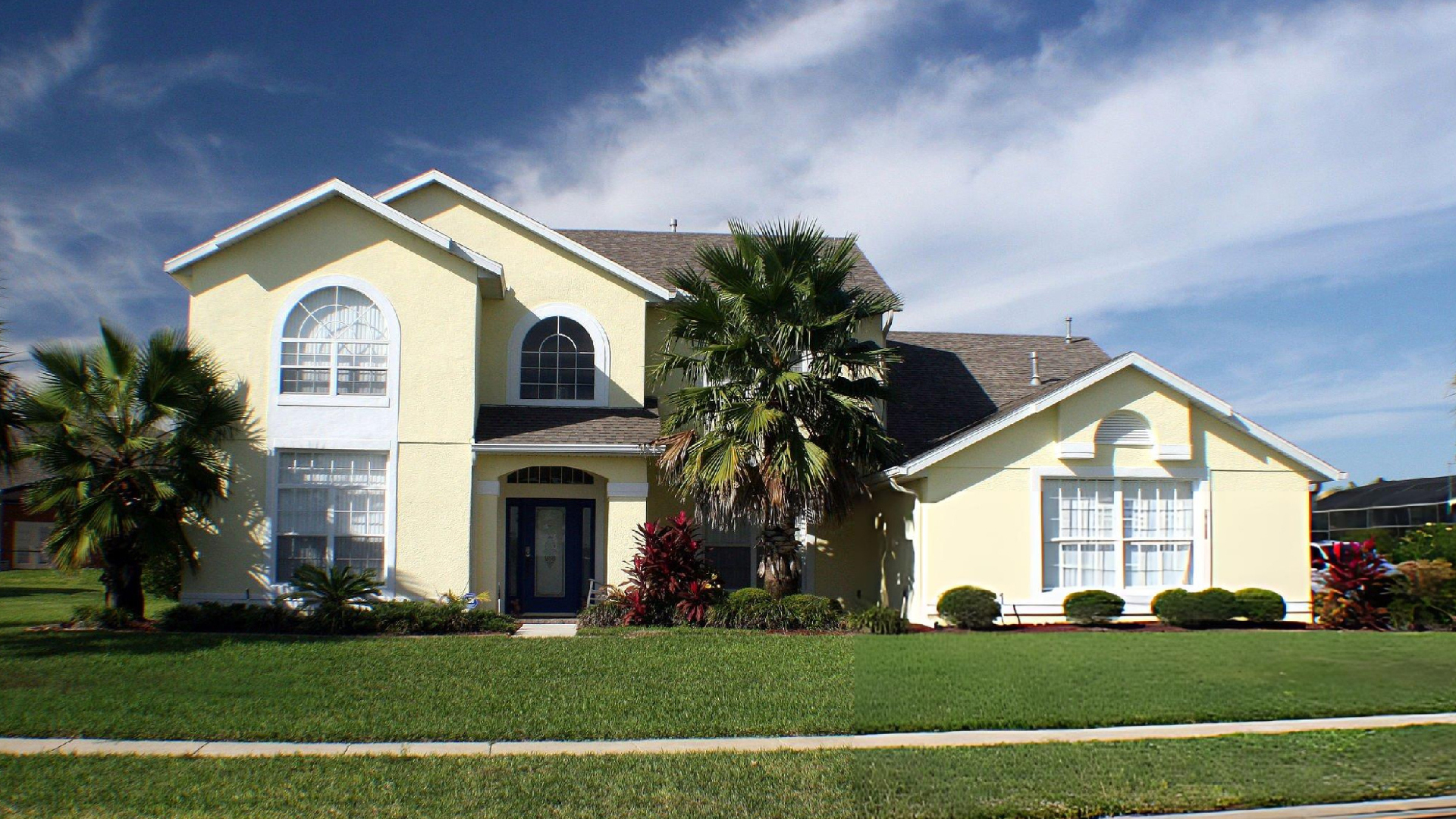 Large modern suburban house with palm trees, manicured lawn, and bright blue sky outside on display.