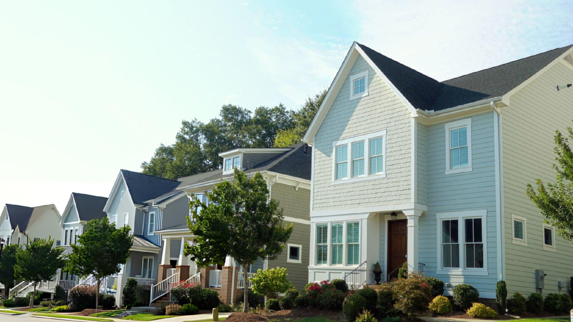 Row of colorful two-story suburban homes with landscaped yards, trees, and pathways under bright daylight sky. Row of colorful two-story suburban homes with landscaped yards, trees, and pathways under bright daylight sky.