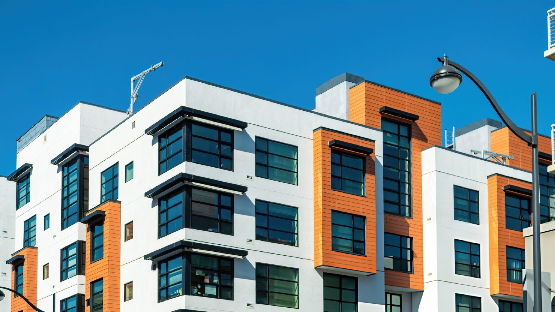 Modern white and orange apartment building exterior with large windows, street lamp, and bright blue sky. Modern white and orange apartment building exterior with large windows, street lamp, and bright blue sky.