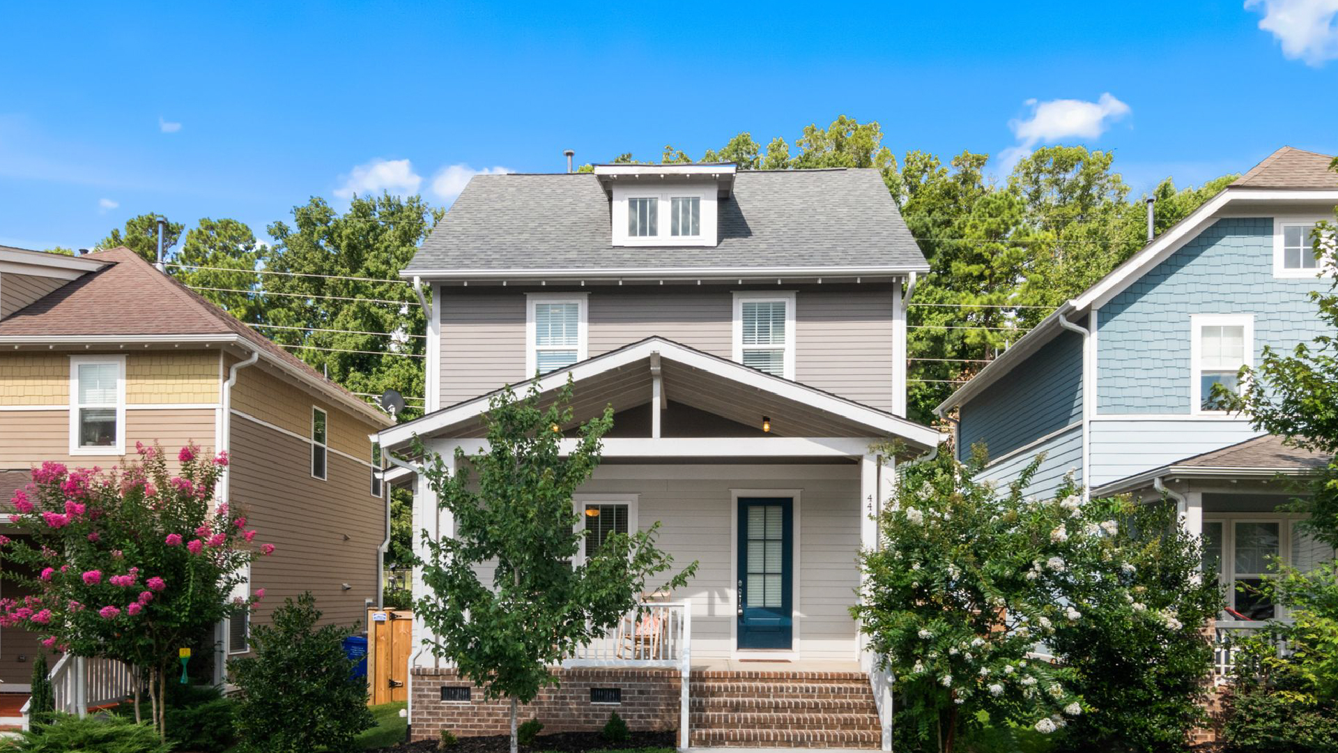 Gray two-story house with white porch, brick steps and blooming crape myrtles under a bright blue sky. Gray two-story house with white porch, brick steps and blooming crape myrtles under a bright blue sky.