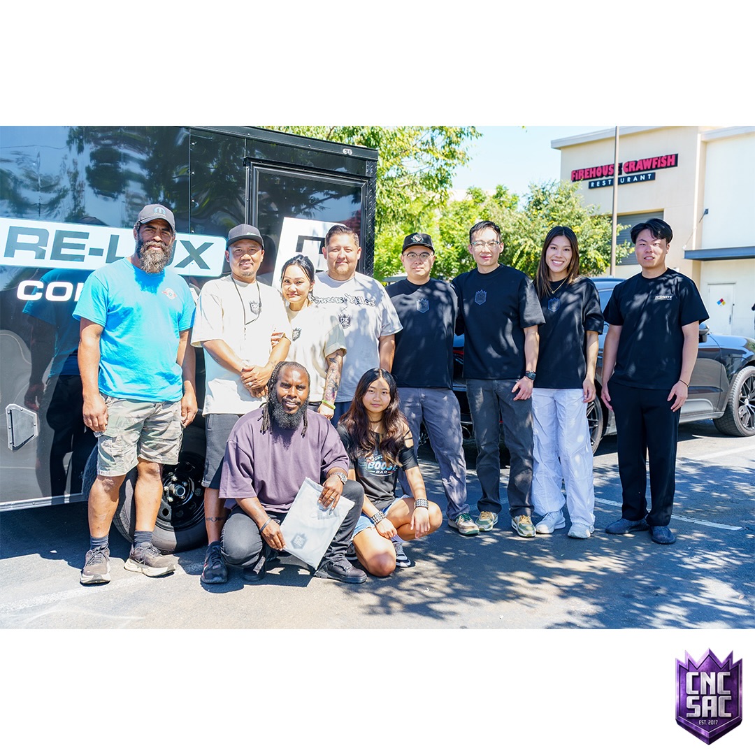 Group of attendees posing together in front of a sponsor banner at a Cars and Coffee Sac event