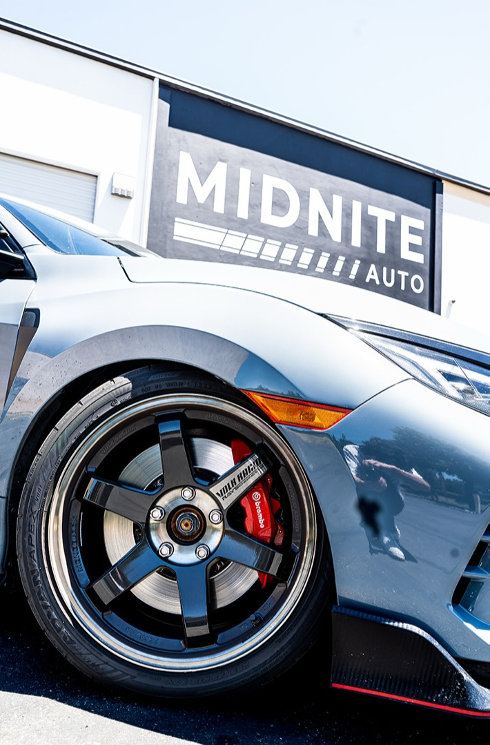 Front wheel and fender of a silver Honda Civic Type R with red brake calipers