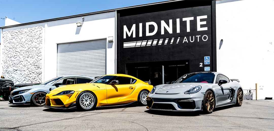 Yellow Toyota Supra and a silver Porsche parked outside an auto shop