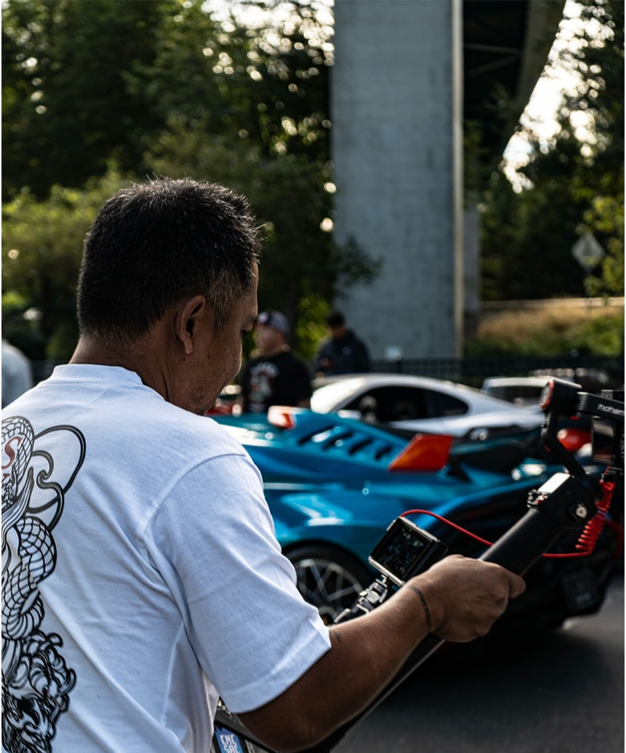 Attendee filming a blue car with a handheld gimbal camera at an event