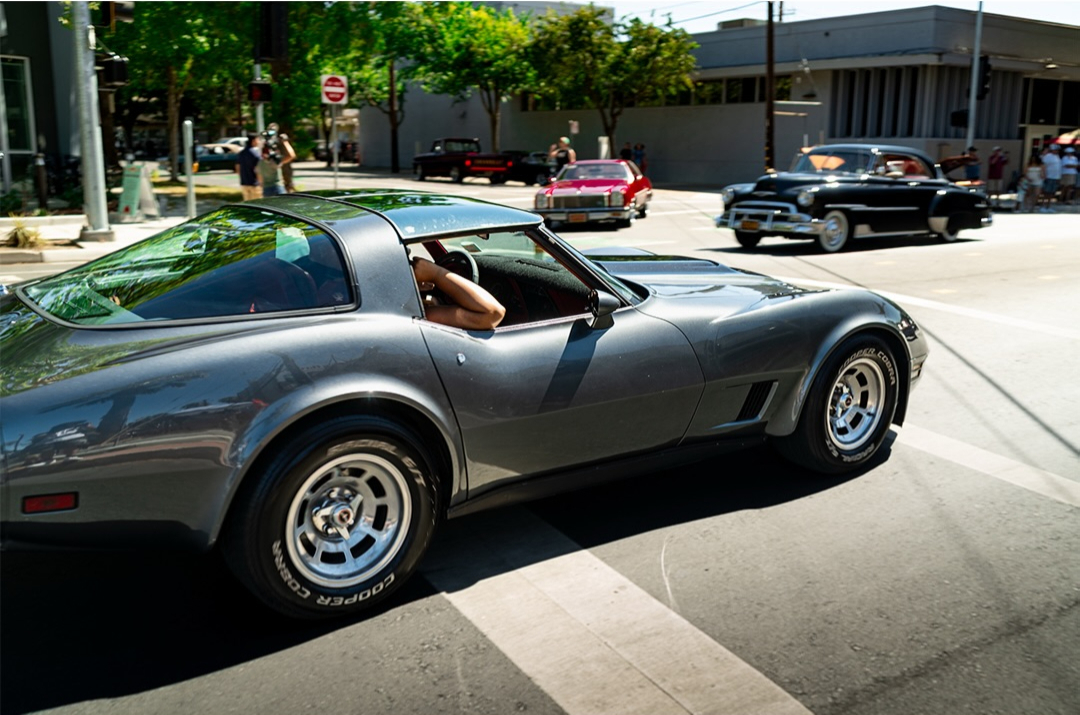 Silver Chevrolet Corvette driving along a city street
