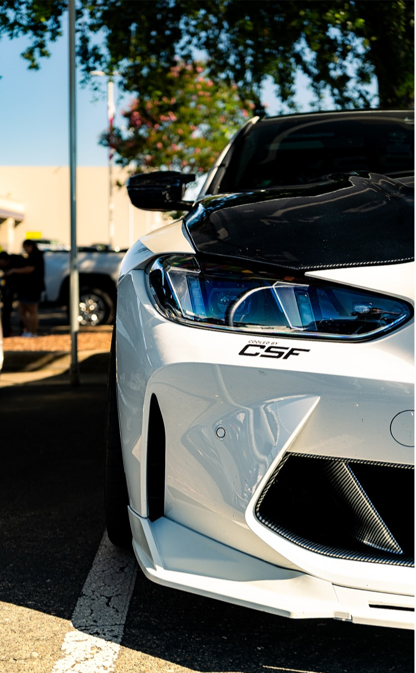 Front of a white car with a carbon fibre hood at an outdoor event