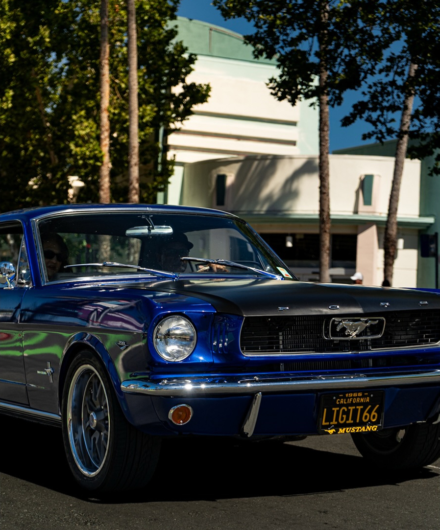 Blue classic Ford Mustang parked under trees