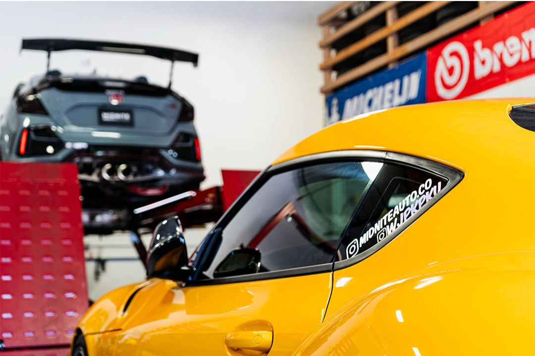 Yellow and black cars with rear wings parked inside a workshop hung with sponsor banners