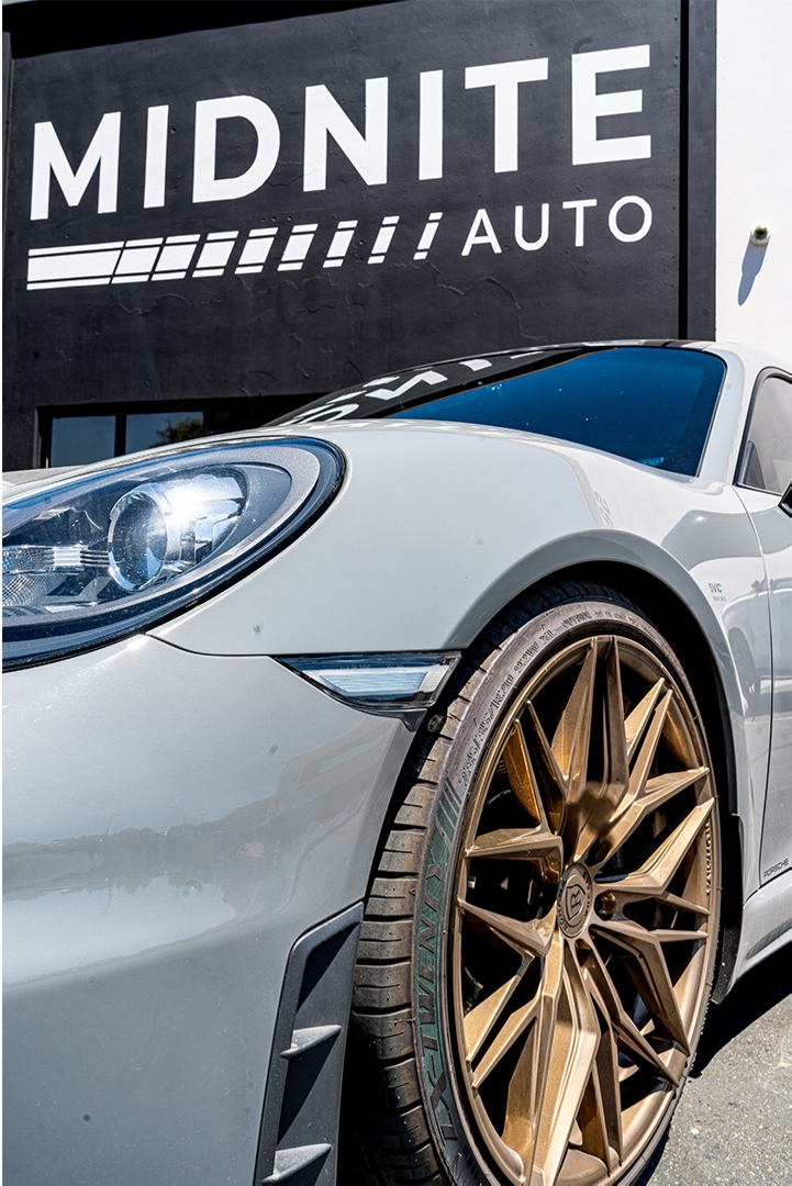 Front quarter of a silver Porsche on bronze wheels parked outside a shop