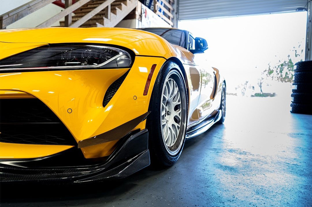 Front quarter of a yellow Toyota Supra inside a workshop