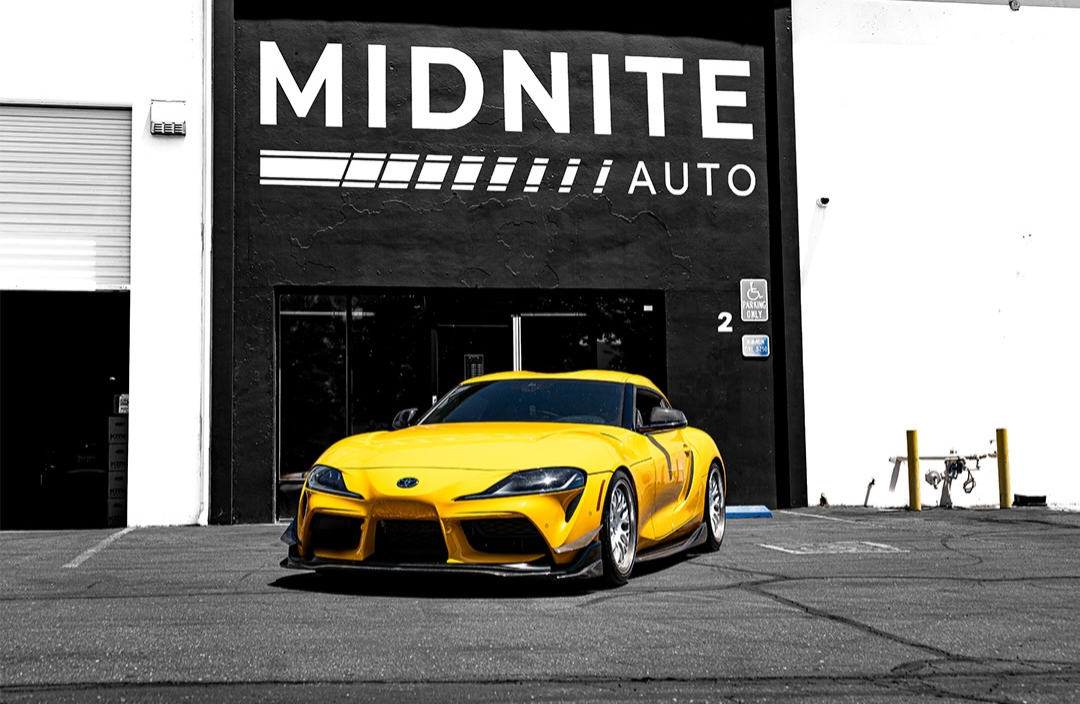 Yellow Toyota Supra parked in front of an auto shop building