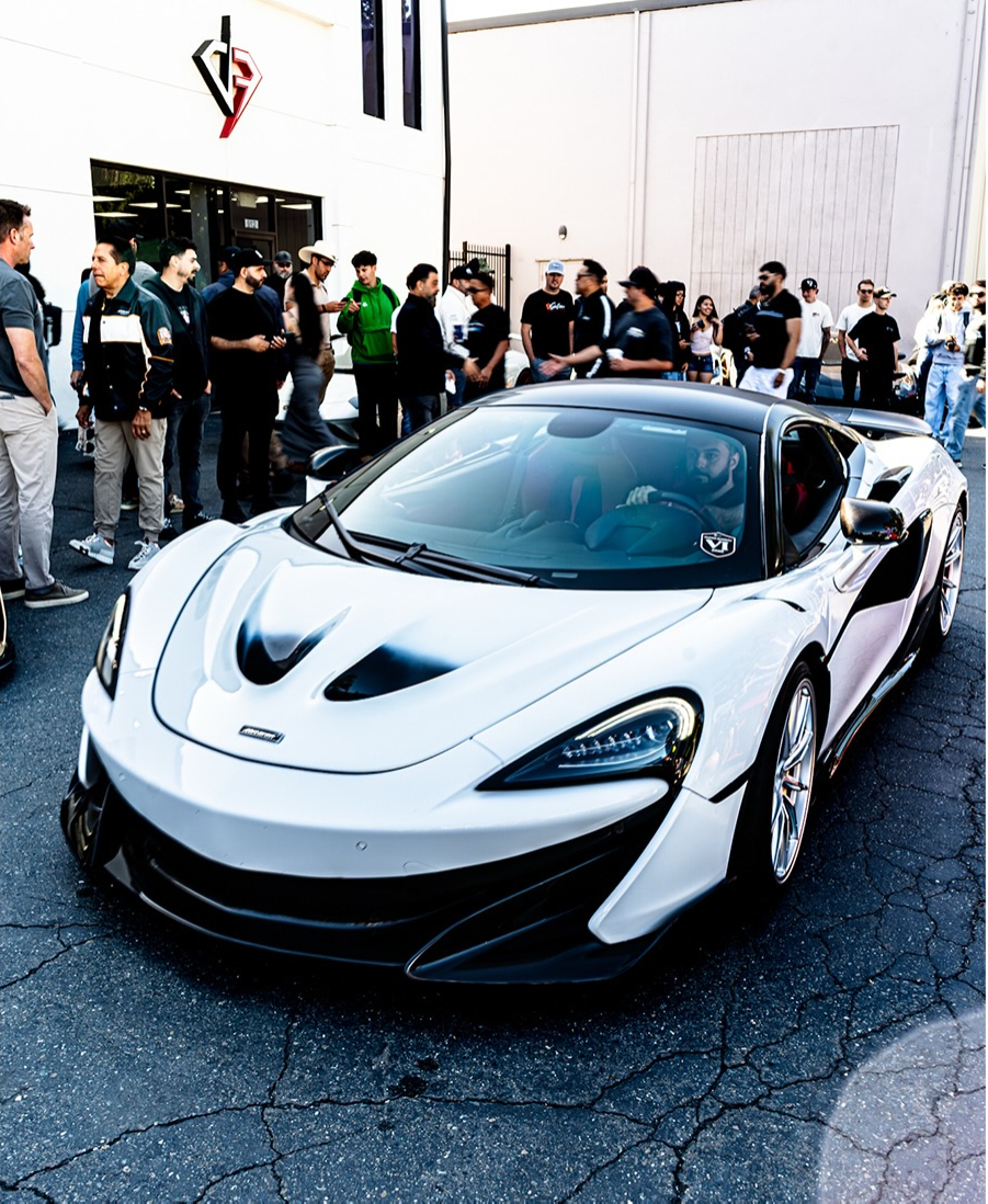 White McLaren with a crowd of attendees gathered behind it at an indoor venue