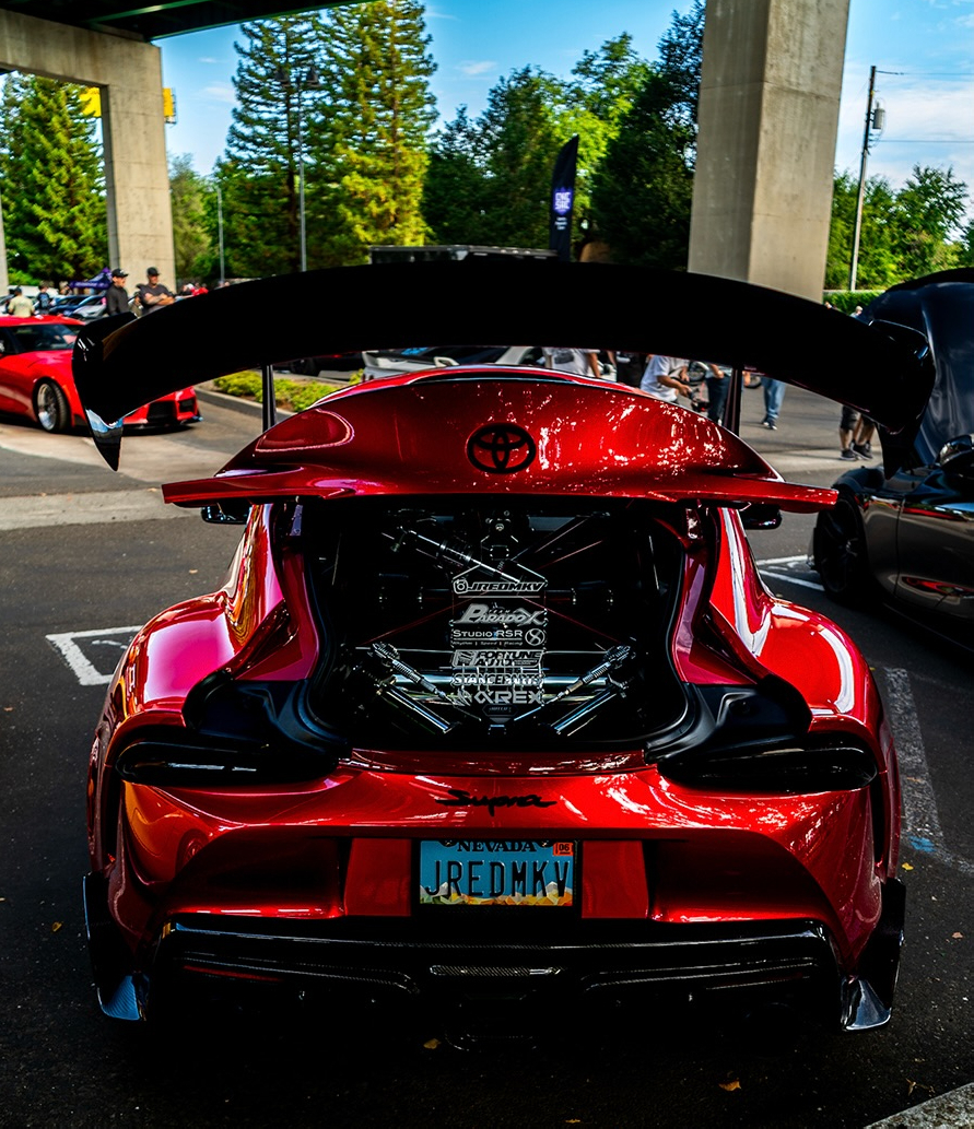 Rear of a red Toyota Supra with a large wing and centre exhaust parked at an event