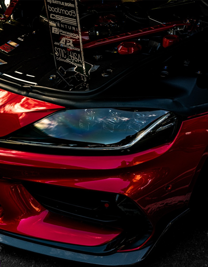 Close up of a red cars headlight with the hood raised above it