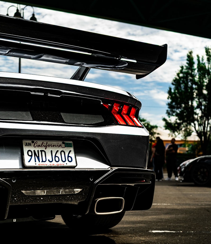 Rear of a dark car fitted with a large swan neck rear wing at an event
